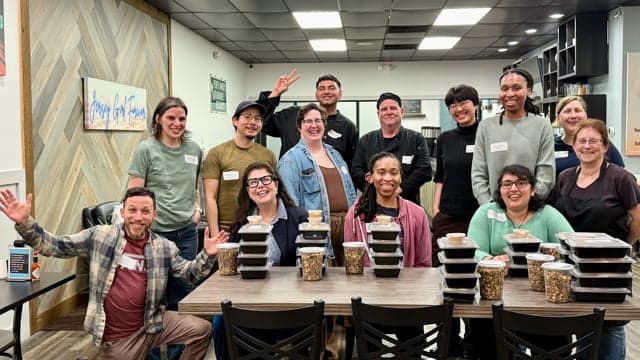 Smiling young people preparing large bowls of chopped vegetables in a community kitchen.