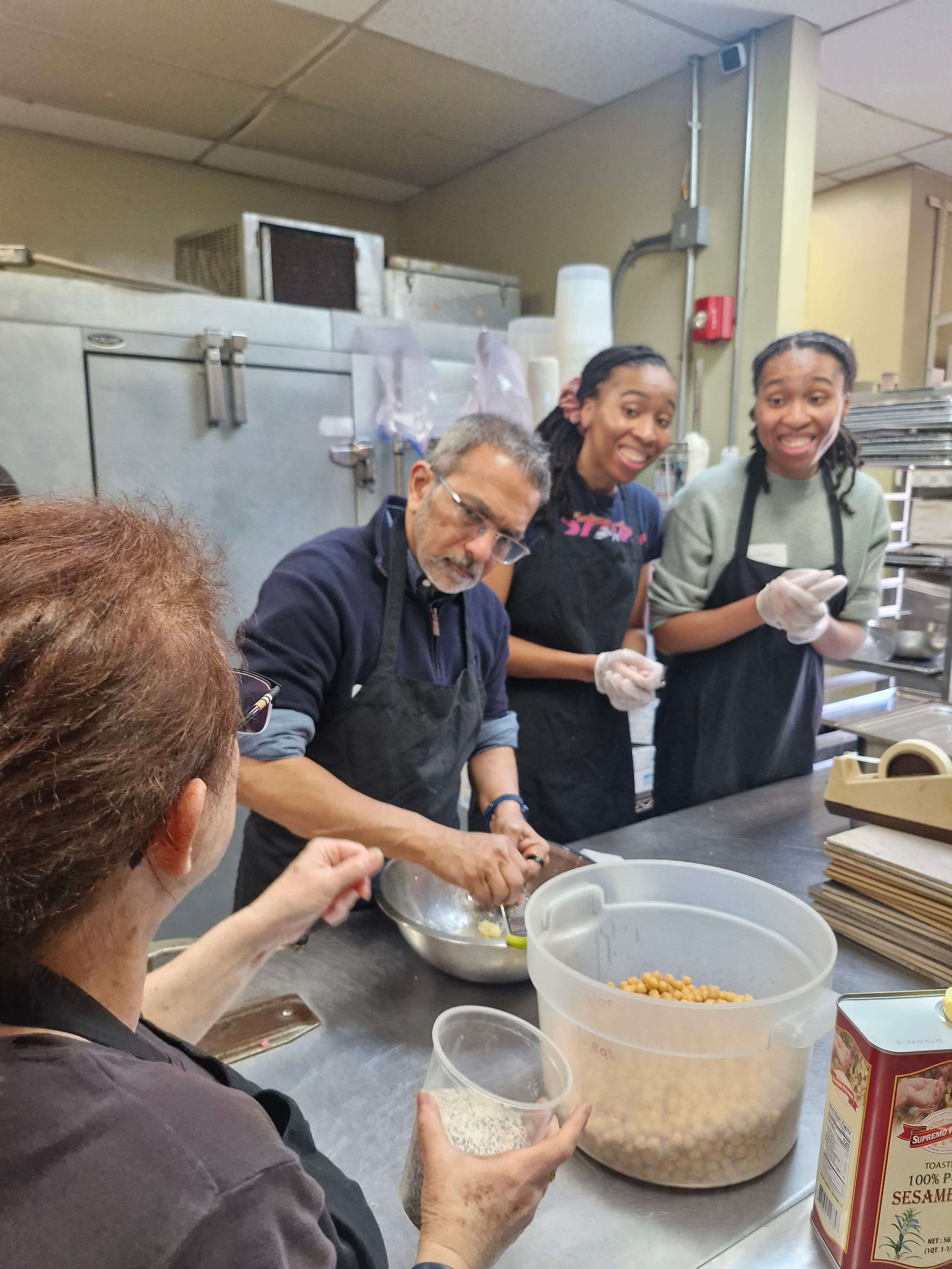 Diverse group of people wearing aprons and gloves preparing chickpeas in a commercial kitchen.