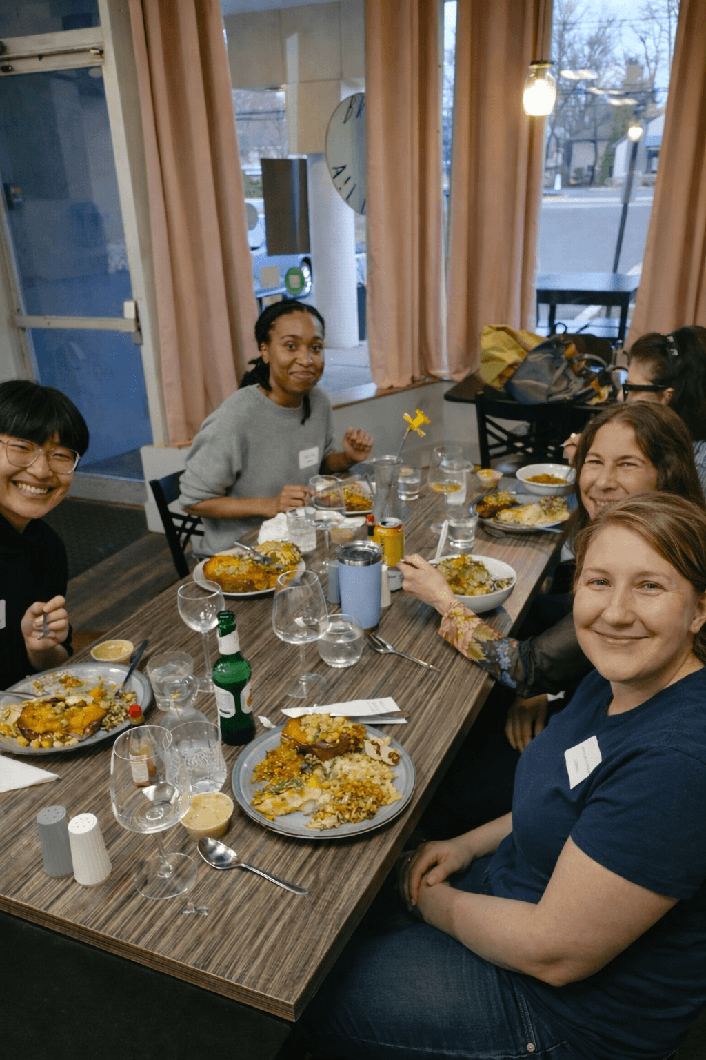 Diverse group of smiling women share a meal at a wooden table in a restaurant.